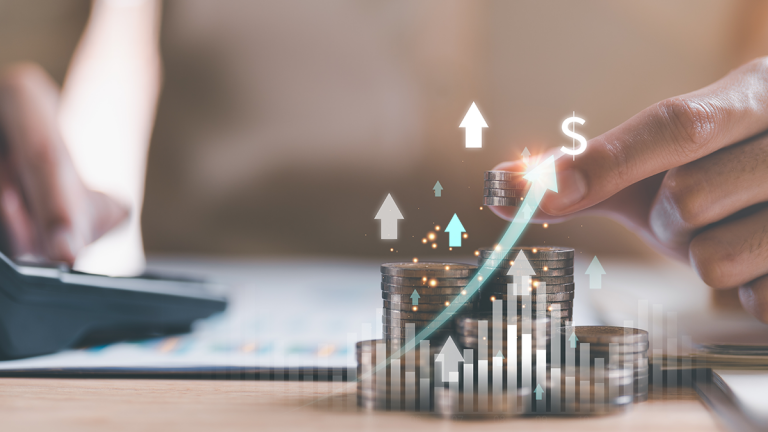 Käsi pinoaa kolikoita, taustalla näkyy laskin ja ylöspäin osoittavia nuolia sekä kasvava graafi – kuva symboloi kustannusten tai tuoton nousua.