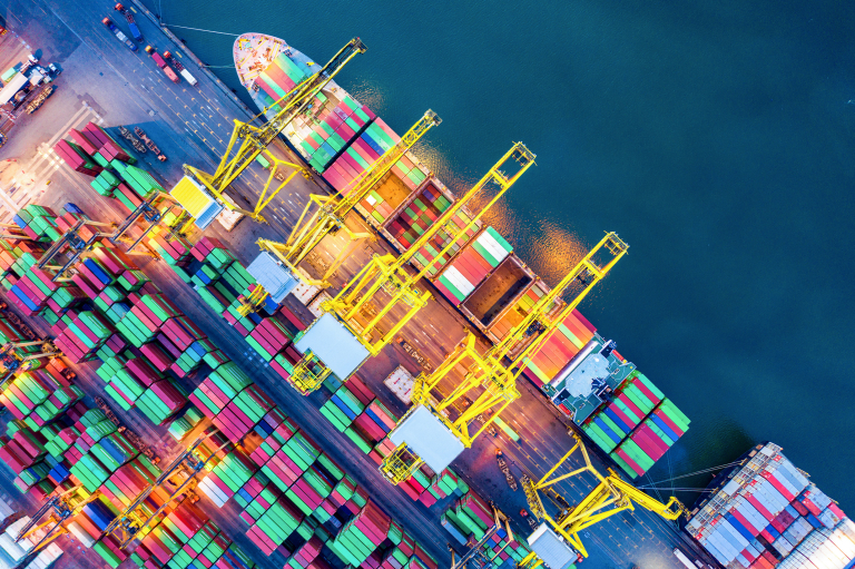 Ilmakuva konttisatamasta, jossa värikkäitä rahtikontteja, nostureita ja laivoja veden äärellä.