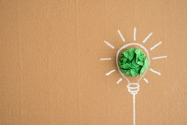 Piirretty hehkulamppu pahvisella taustalla, jossa vihreä paperipallo symboloi ympäristöystävällistä ideaa.
