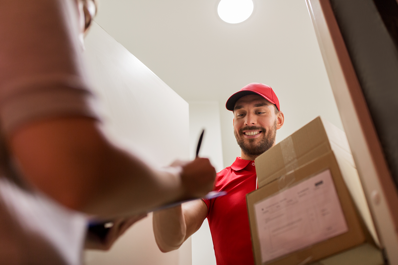 En kurir levererar ett paket och ber mottagaren att kvittera leveransen vid dörren.